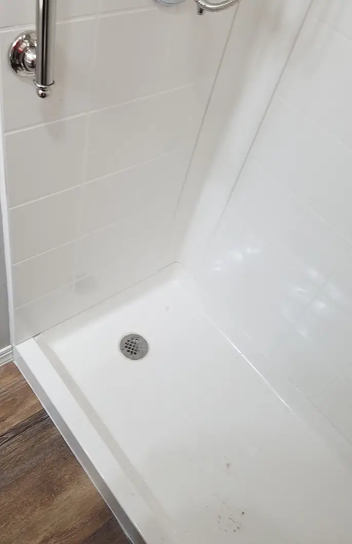 A shite shower with a covered drain and white tiling