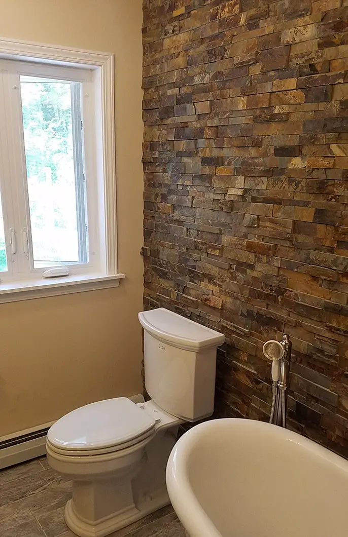 A bathroom with a white toilet, bathtub, and exposed brick