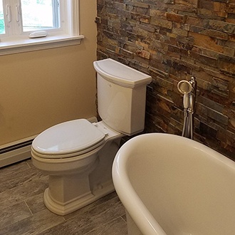 A bathroom with a white toilet, bathtub, and exposed brick