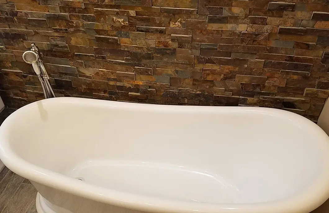 A white bathtub with a brick stone wall