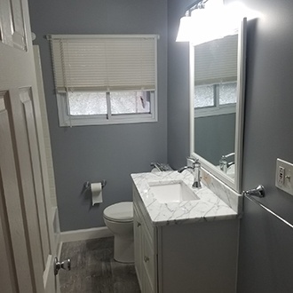 A bathroom with gray-blue walls, marble countertop, and white cabinets