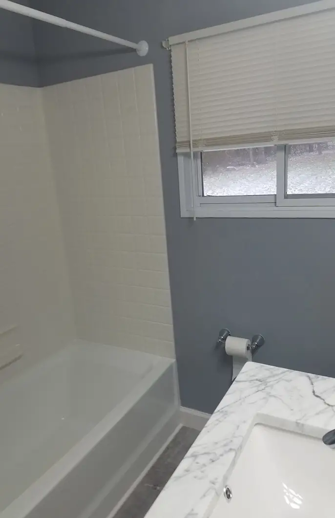 A bathroom with a marble countertop, white tiling, and white bathtub
