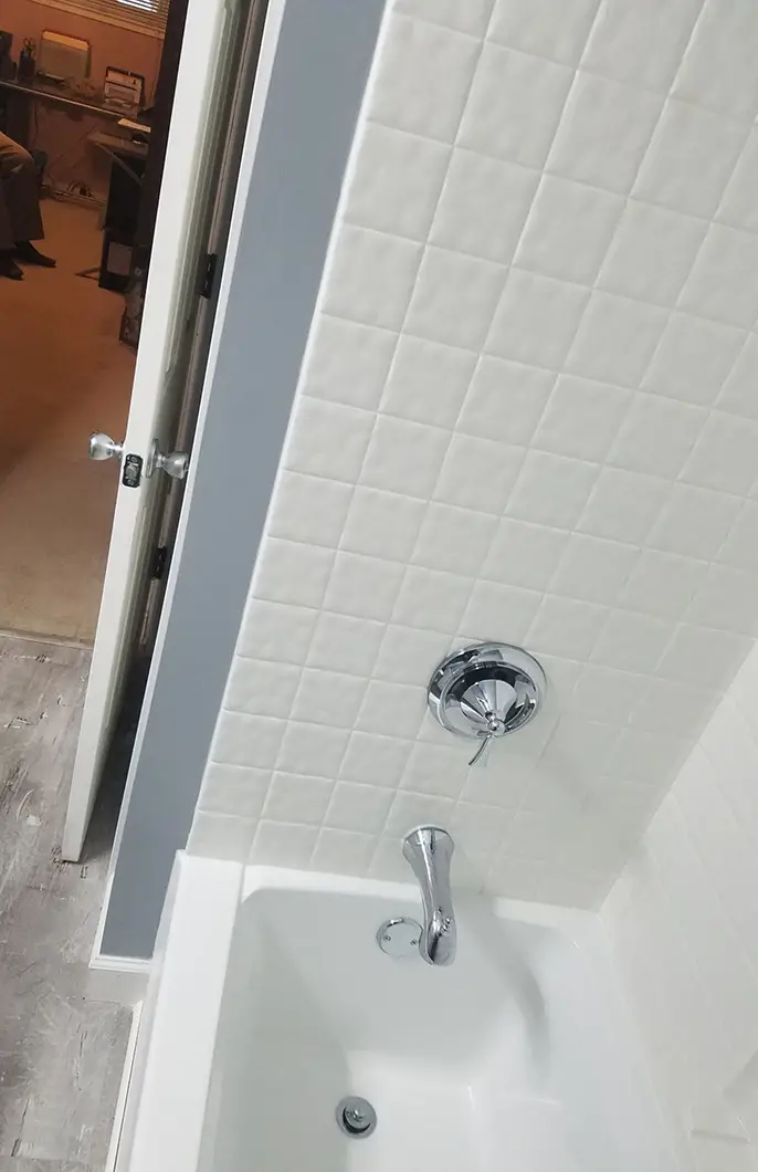 A shower with a steel faucet and white tiling
