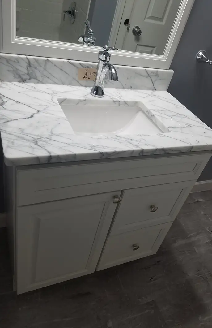 A marble bathroom counter with white cabinets and a steel faucet