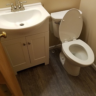 A bathroom with white cabinets, a steel sink faucet, and a porcelain toilet