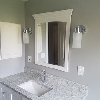 A bathroom with a stone countertop, steel sink faucet, and white cabinets