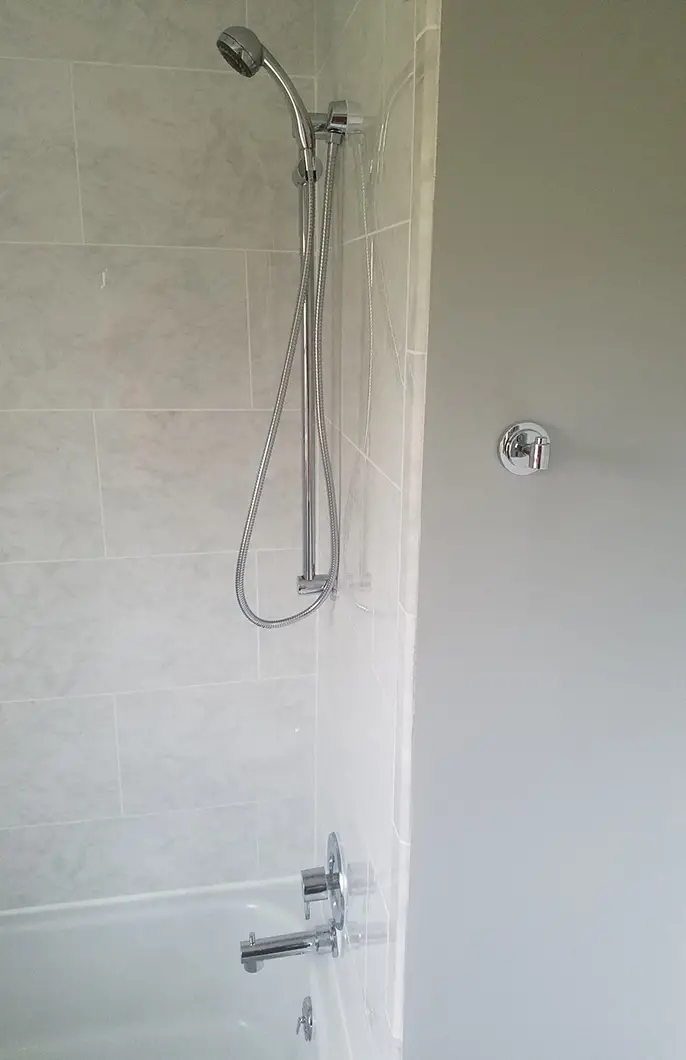 A gray-tiled shower with a removable showerhead and steel faucet