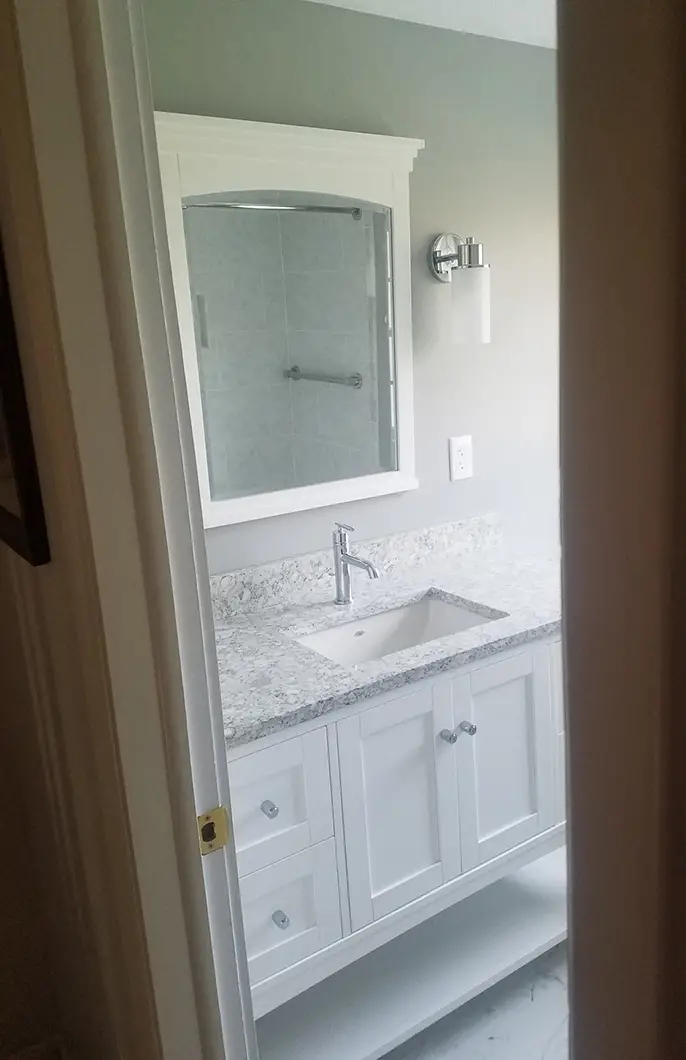 A bathroom with a stone countertop, steel sink faucet, and white cabinets