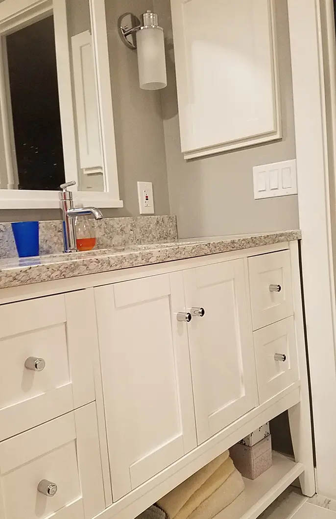 A bathroom counter with gray stone, a steel faucet, and white cabinets