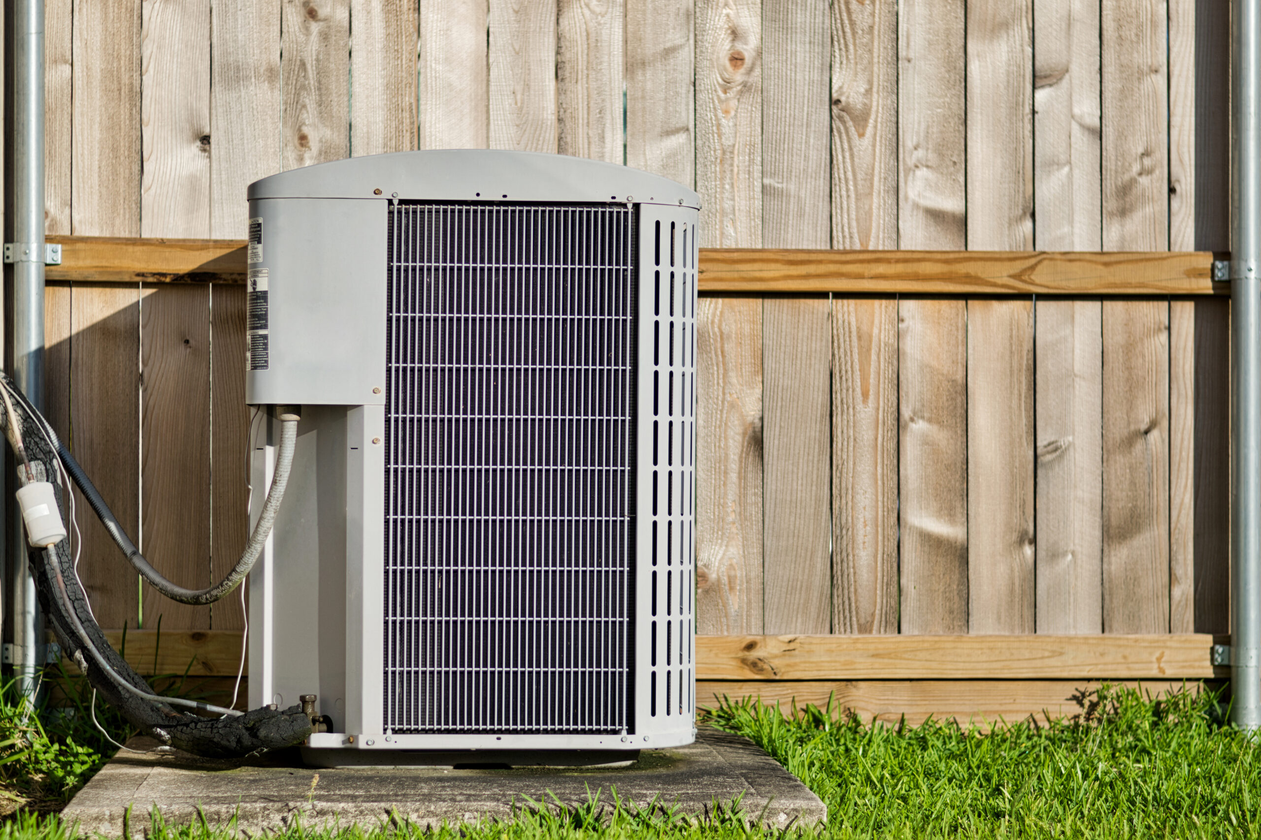Outdoor AC condenser unit against a wood fence